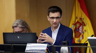 José Pablo López, presidente de RTVE, gesticulando con las manos durante una comparecencia ante la Comisión Mixta de Control Parlamentario, con la bandera de España al fondo